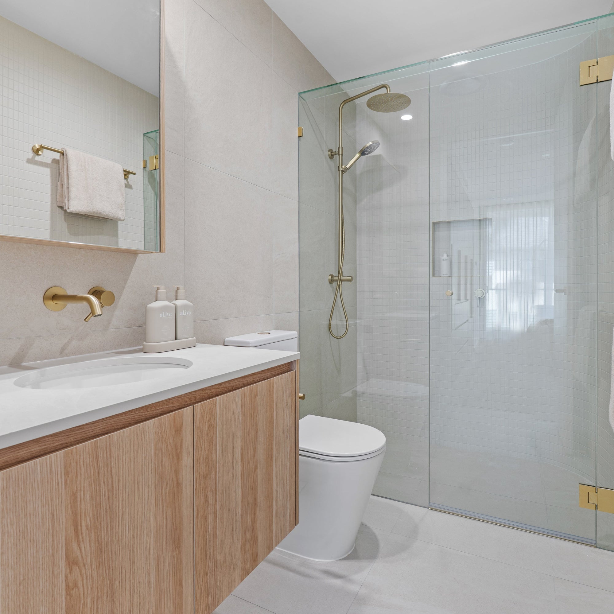 Brushed brass twin rail shower installed in modern bathroom with glass enclosure.